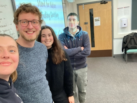 Four people stand next to a presentation screen, smiling at the camera