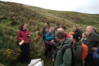 A group standing with a researcher as she explains about Manx Shearwaters. The colony can be seen behind.