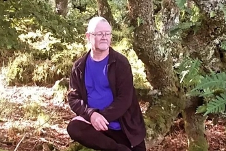Gareth sat on a log in the woods. 