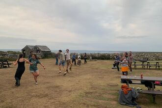 A group of people dancing in the courtyard for the island ceilidh. There are musicians playing to the side.