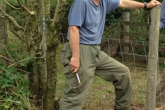 A man leaning on a fence. There are trees in the background.