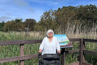 A woman stood with a walking aid on a wooden boardwalk platform in a nature reserve
