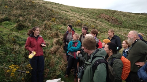 A group standing with a researcher as she explains about Manx Shearwaters. The colony can be seen behind.