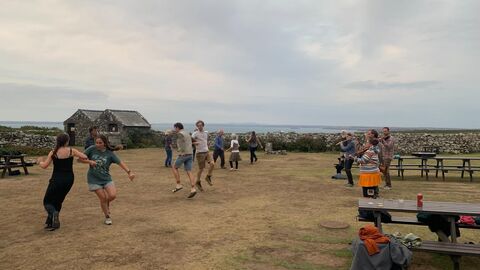 A group of people dancing in the courtyard for the island ceilidh. There are musicians playing to the side.