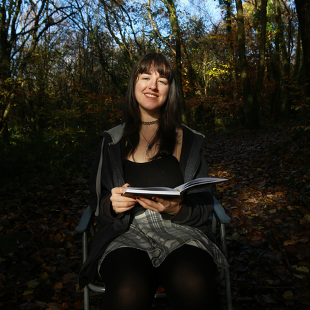 Women sat on chair outside holding a book.