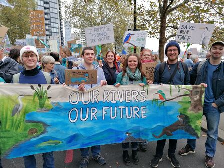 A group of young people in a crowd at the March for Water event. They are holding a big banner which says 'our rivers, our future' and placards that read 'Save Our Taff'..