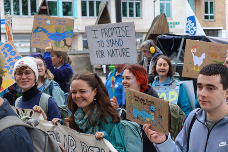 Young people in a crowd at the March for Water event. They read signs that say 'I promise to stand for nature'. 