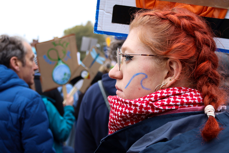 A young woman at the March for Water event in London. She has a wave painted in blue on her cheek.