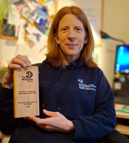 Lisa Morgan, Head of Islands and Marine Conservation, holding the Dame Mary Smeiton Award which reads 'Skomer and Skokholm Accessible Boat Trips' and features the Wildlife Trust logo. 