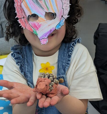 A child wearing a hedgehog shaped mask and holding a handmade clay model of a hedgehog.