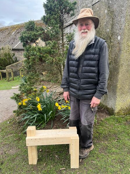 A man with a long white beard stood next to a small wooden table