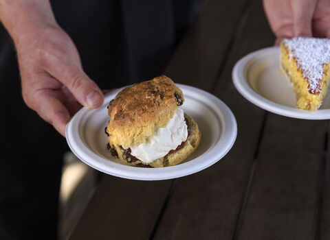 A scone and cake on plates being served by someone. 